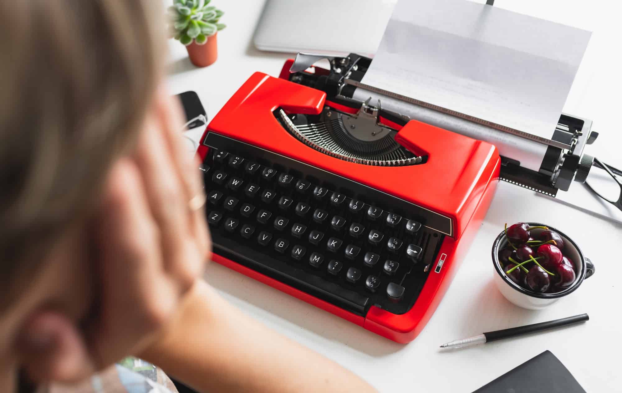 Woman writer thoughtfully working on a book on her Desk red typewriter