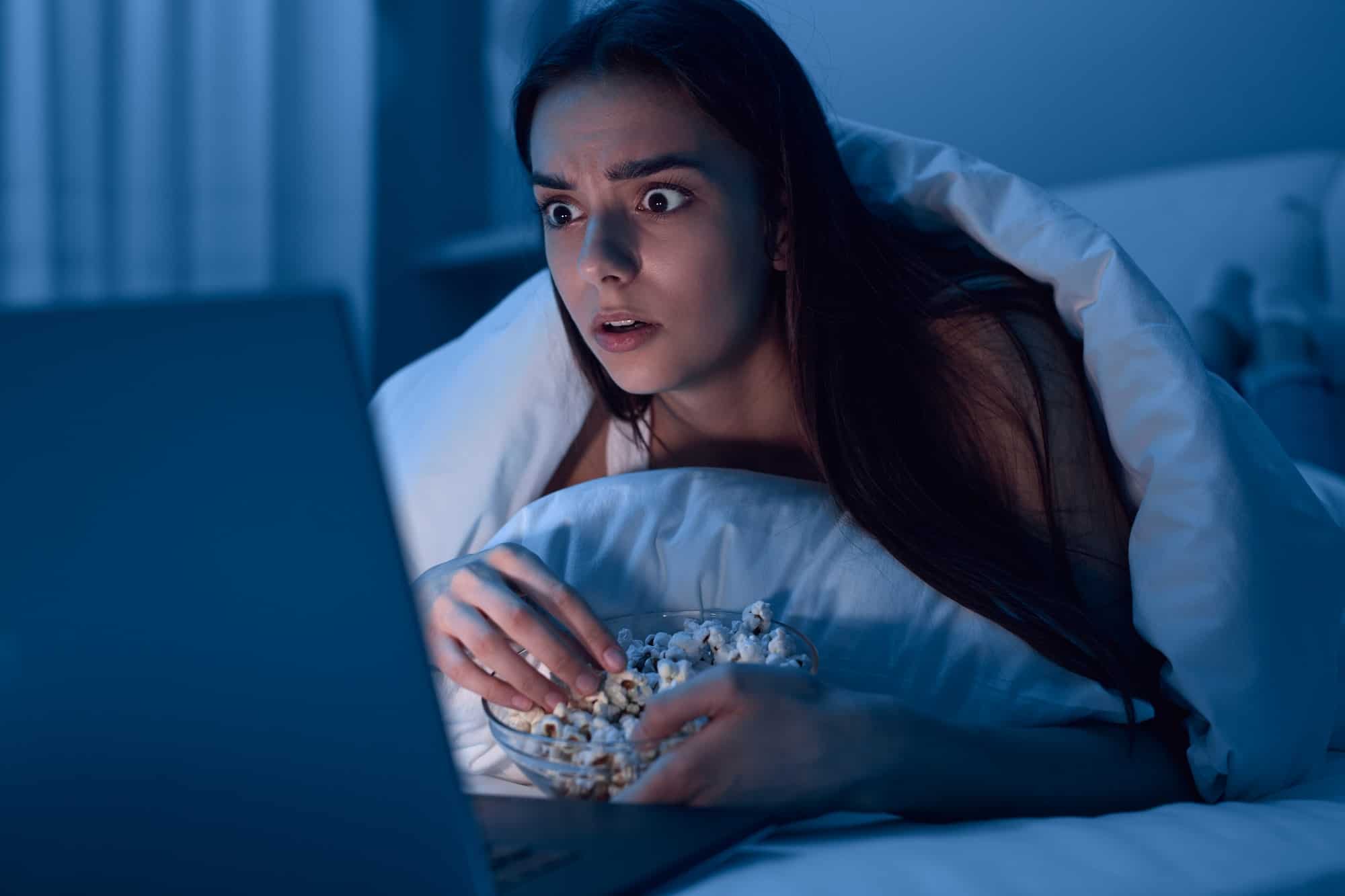 Woman watching movie and eating popcorn at night